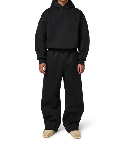 Person wearing a black hoodie and pants on a white background