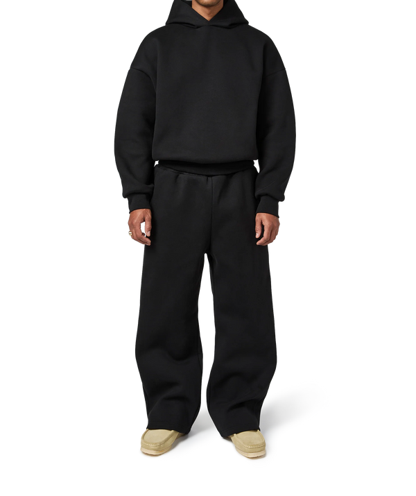 Person wearing a black hoodie and pants on a white background